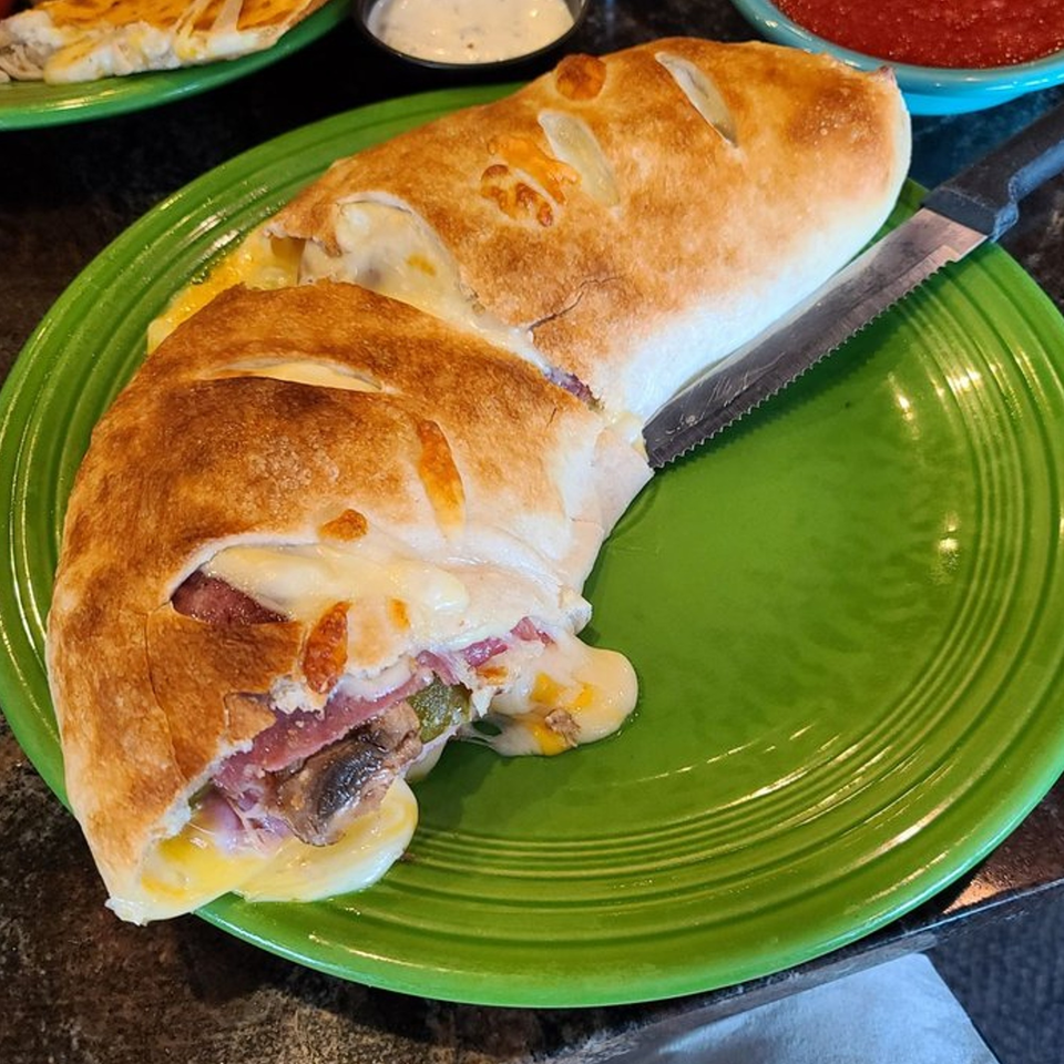 A calzone with melted cheese, ham, and mushrooms, served on a green plate with a knife.