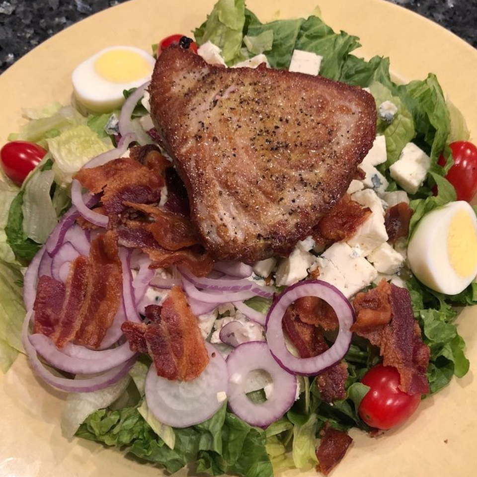 A Lisa's Cafe American salad with seared tuna, bacon, red onion, cherry tomatoes, and hard-boiled egg.