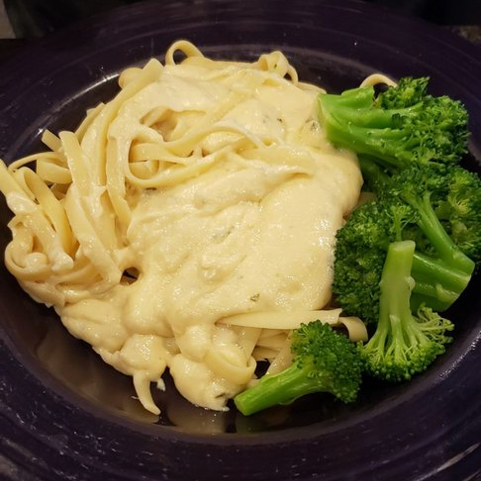 Creamy fettuccine alfredo with fresh green broccoli florets served on a dark plate.