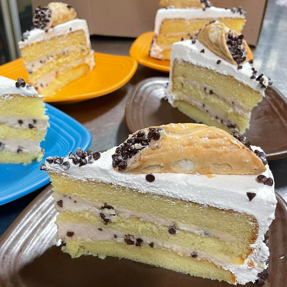 Slices of Lisa's Cafe cannoli cake with white frosting and chocolate chips on colorful plates.